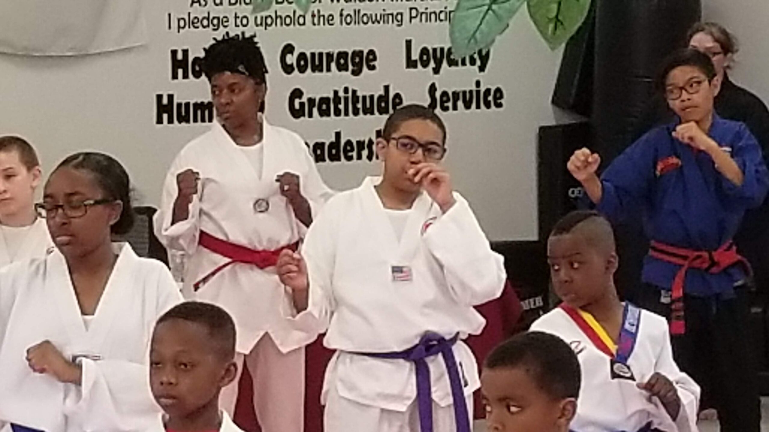 Martial arts students seated on mats participate in a structured class activity within the training space.