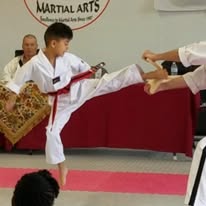 Martial arts student executes a controlled kick toward a handheld target during practice.