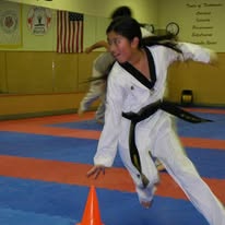 Martial arts student practices a high kick over training cones during a class session.