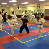 Martial arts students practice coordinated techniques together on red and blue mats inside the studio.