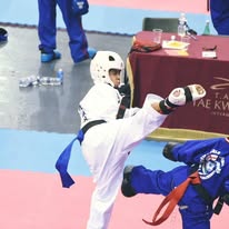 Martial arts student executes a high kick toward a padded target during a class drill.