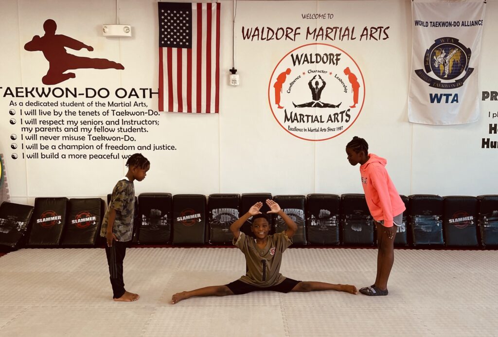 Martial arts students seated on mats participate in a structured class activity within the training space.