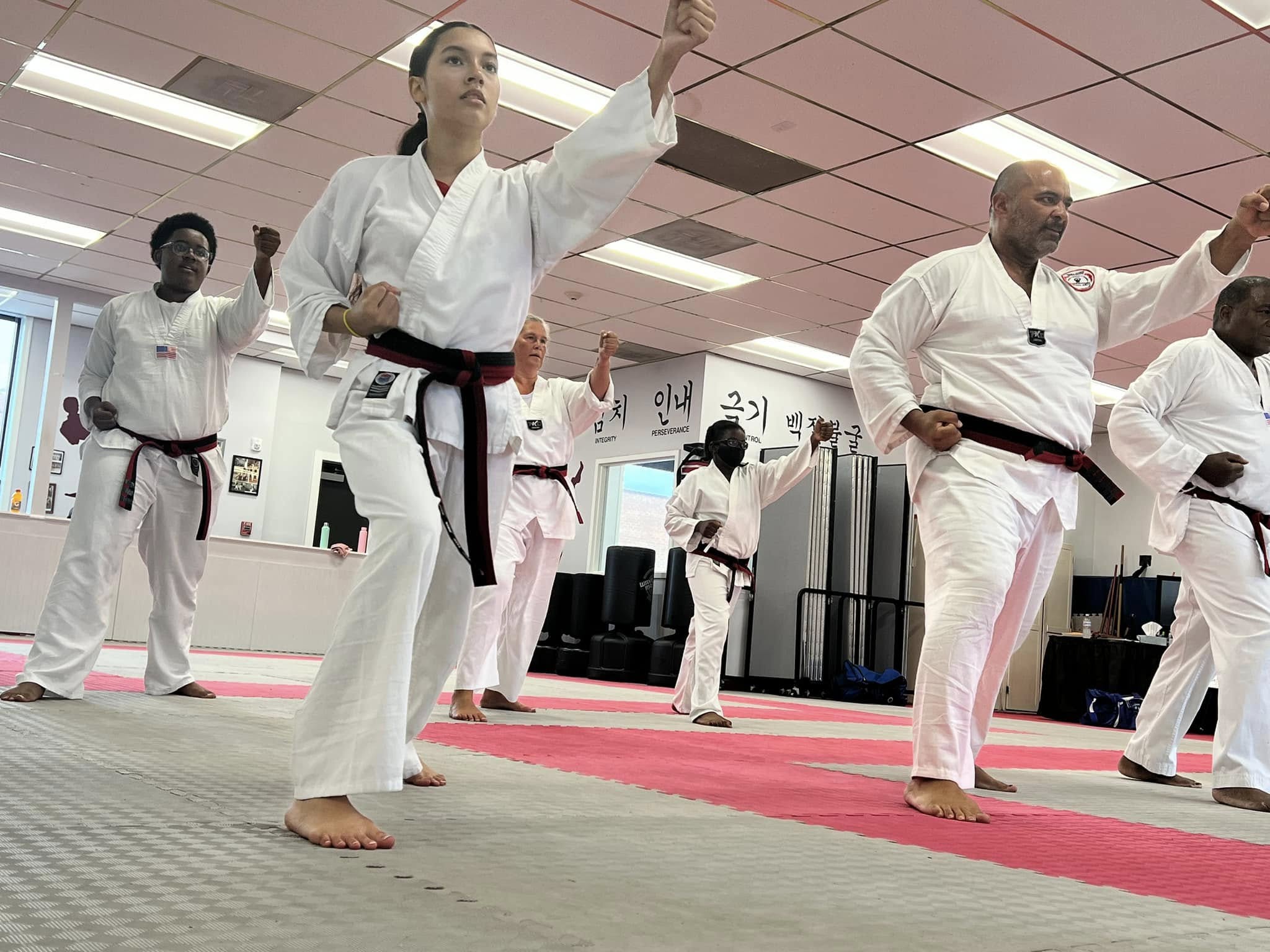 Martial arts students seated on mats participate in a structured class activity within the training space.