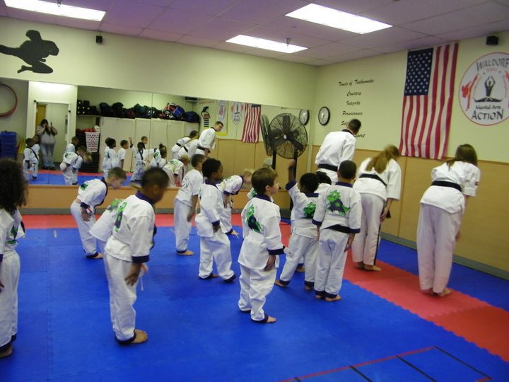 Martial arts students seated on mats participate in a structured class activity within the training space.