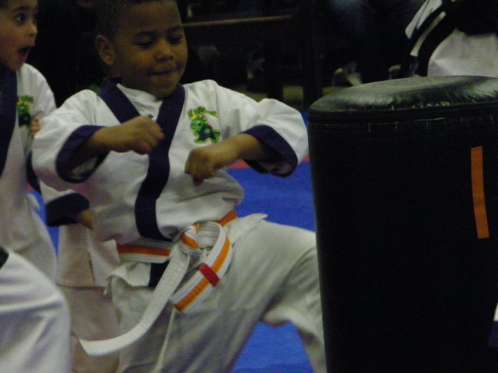 Students practice coordinated martial arts movements together on padded flooring inside the dojo.