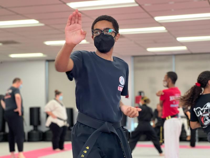 Martial arts students seated on mats participate in a structured class activity within the training space.