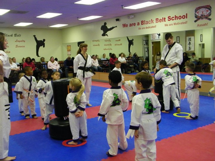 Young martial arts students sit in rows on mats listening during a class session inside the studio.