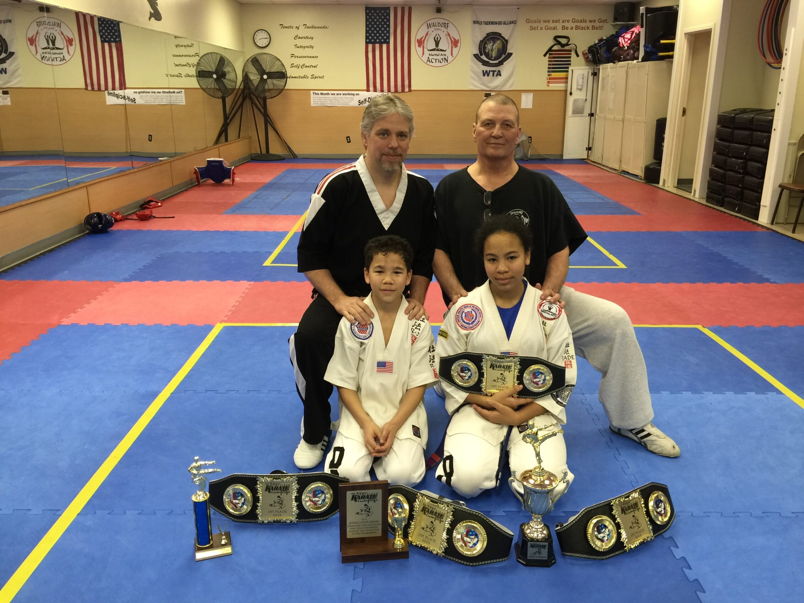 Martial arts students seated on mats participate in a structured class activity within the training space.