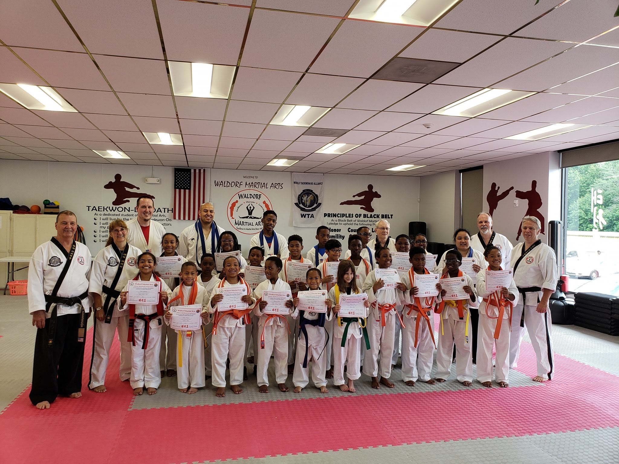 Martial arts students seated on mats participate in a structured class activity within the training space.