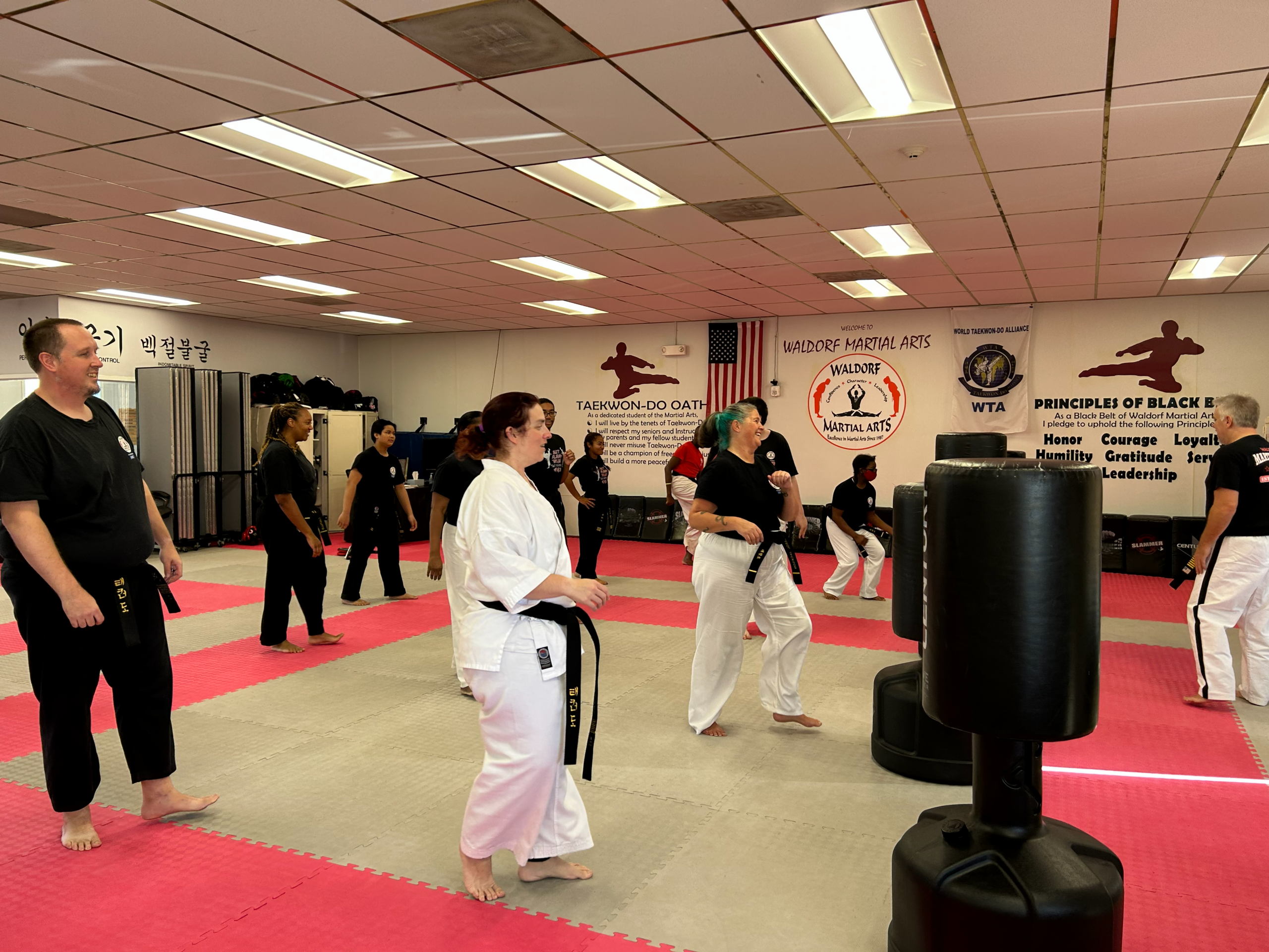 Martial arts students seated on mats participate in a structured class activity within the training space.