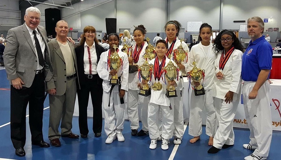 Martial arts students seated on mats participate in a structured class activity within the training space.