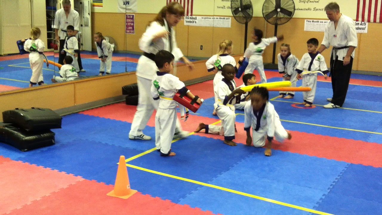 Martial arts students seated on mats participate in a structured class activity within the training space.