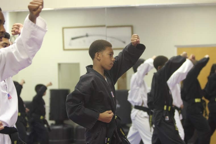 Martial arts students seated on mats participate in a structured class activity within the training space.