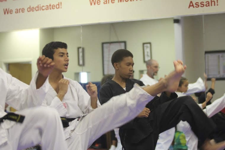 Martial arts students seated on mats participate in a structured class activity within the training space.