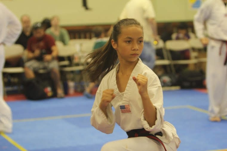 Martial arts students seated on mats participate in a structured class activity within the training space.