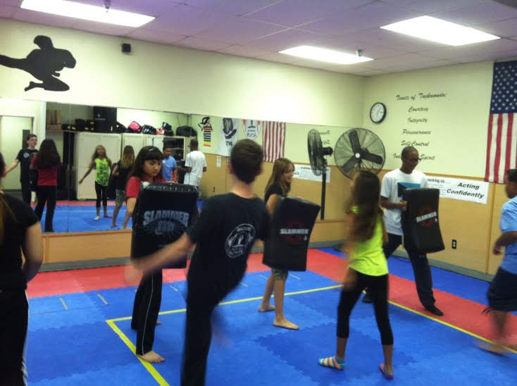 Martial arts students seated on mats participate in a structured class activity within the training space.