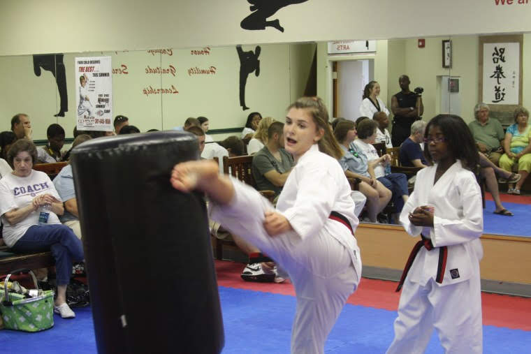 Martial arts students seated on mats participate in a structured class activity within the training space.