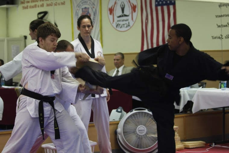 Martial arts students seated on mats participate in a structured class activity within the training space.