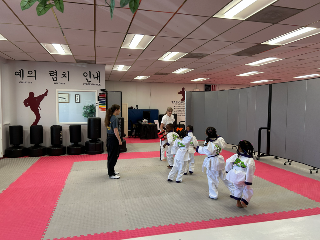Martial arts students seated on mats participate in a structured class activity within the training space.