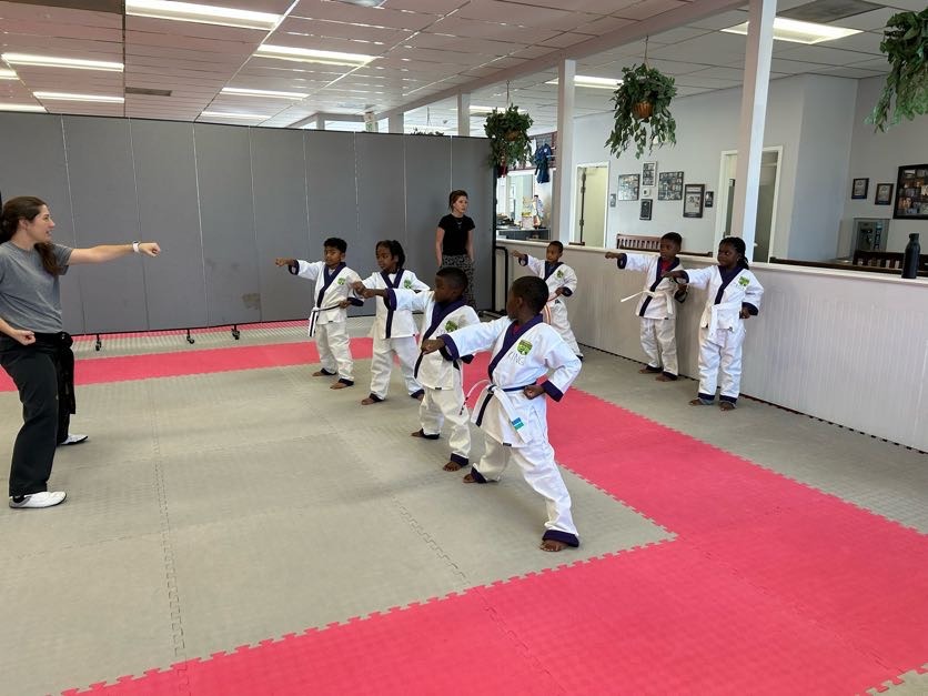 Martial arts students seated on mats participate in a structured class activity within the training space.