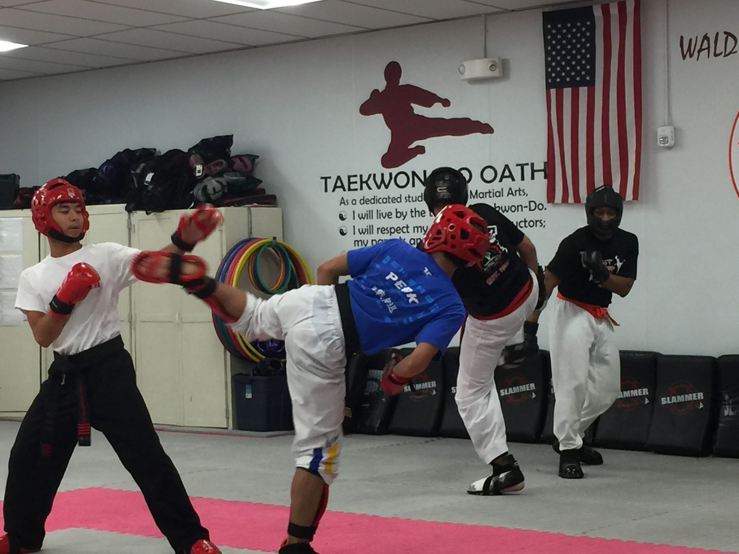 Students wearing protective headgear practice sparring techniques under instructor supervision inside the martial arts studio.