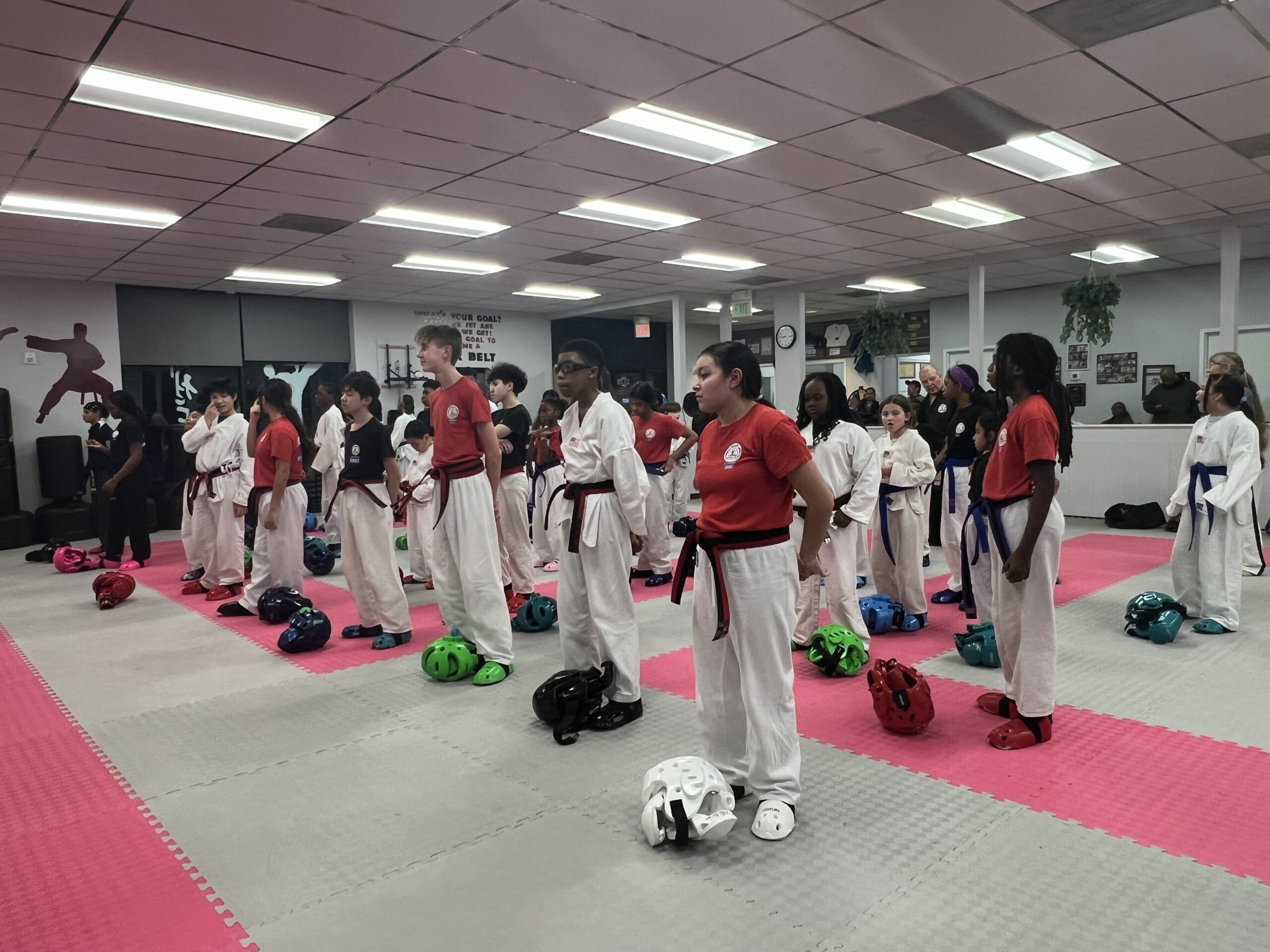 Martial arts students seated on mats participate in a structured class activity within the training space.