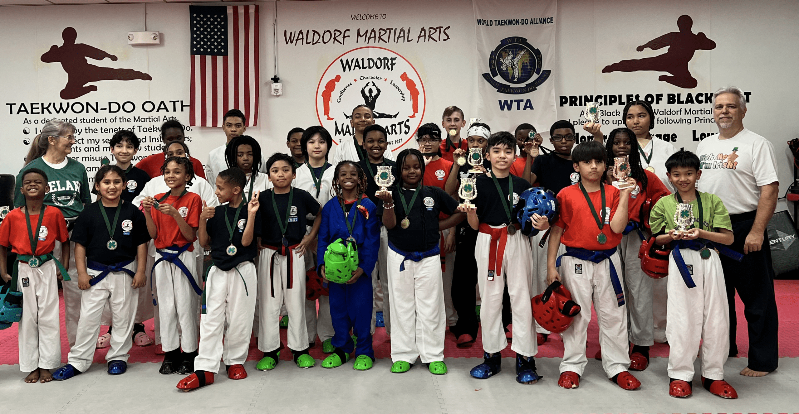 Martial arts students seated on mats participate in a structured class activity within the training space.