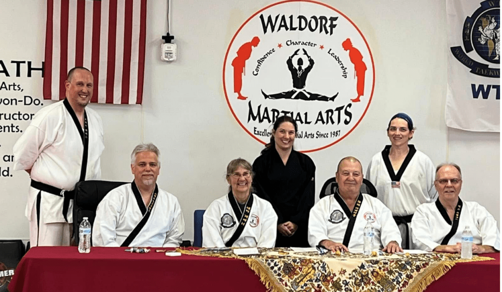 Martial arts students seated on mats participate in a structured class activity within the training space.