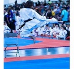 A martial artist executes a high jump kick over a chair at a competition. The audience watches in the background, highlighting the event's intensity.