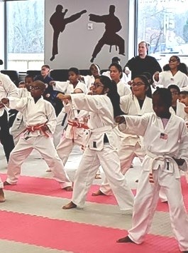 Children in martial arts uniforms practice karate techniques in a dojo, showcasing teamwork and discipline in training sessions.