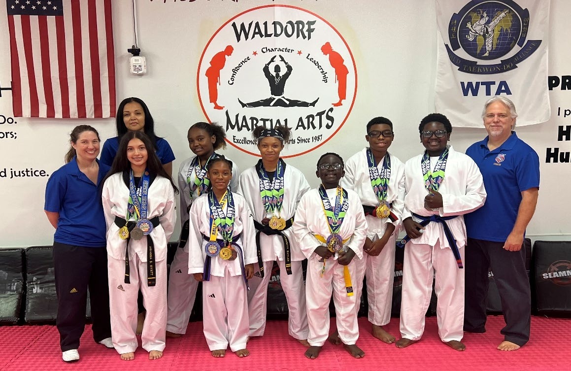 Martial arts students proudly display their medals, flanked by instructors at Waldorf Martial Arts. The group celebrates achievements in taekwondo.